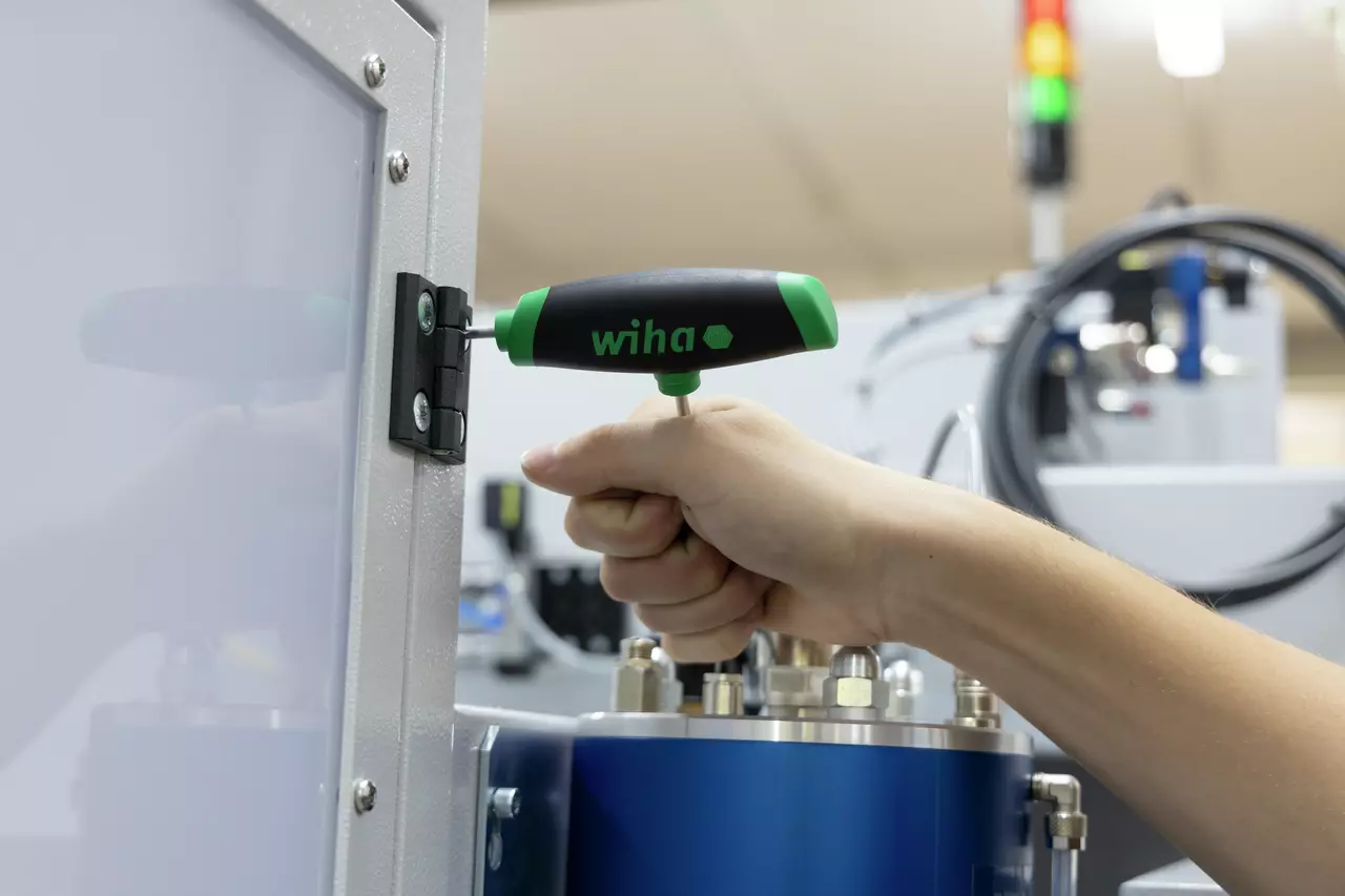 A person using a T-handle screwdriver to adjust a screw on a metal panel in an industrial setting.