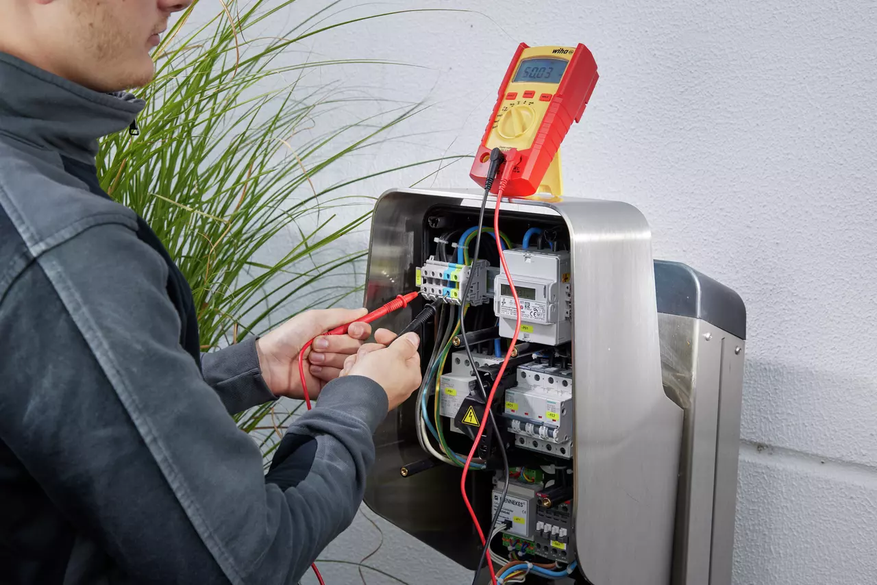 Person using a digital multimeter on an electrical panel outdoors.
