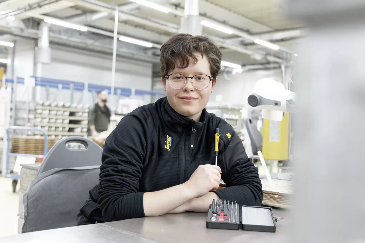 A person sits at a table in a workshop holding a screwdriver. A bit set is in front of them.