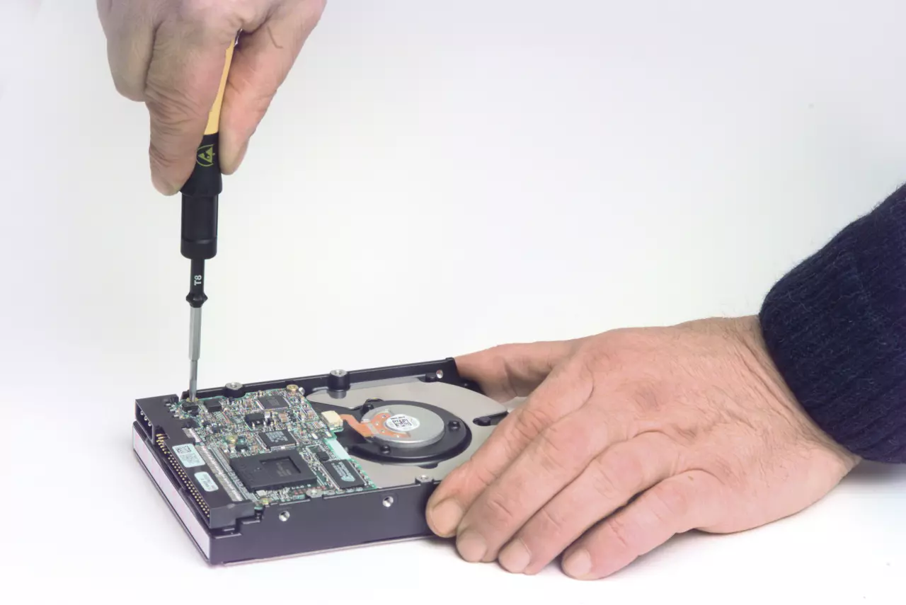A person using a screwdriver on a computer hard drive