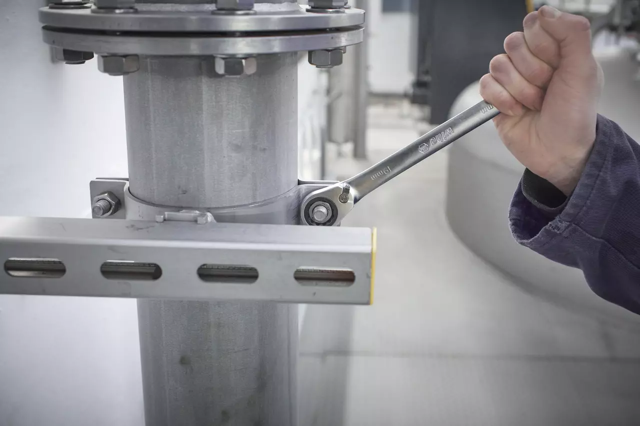 A person using a ratchet wrench on a metal pipe joint.