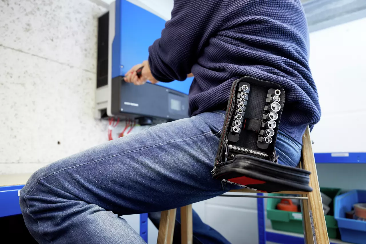 Person working on a device with a socket set nearby on their knee.