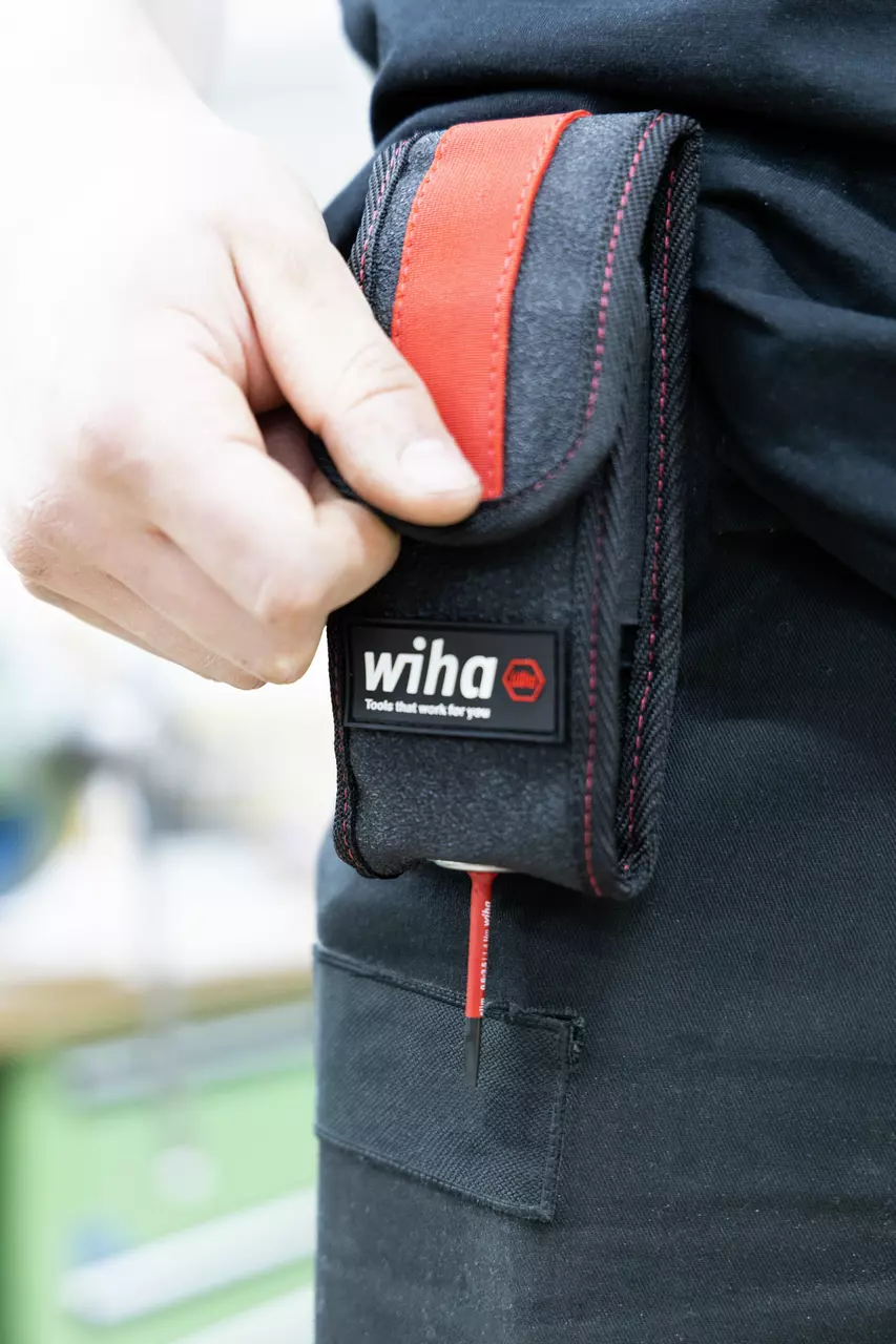 A person holding a black and red tool pouch with a screwdriver inside, attached to a belt.