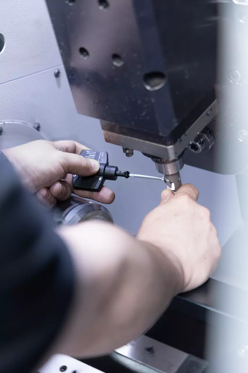 Persoon gebruikt een klein gereedschap op een CNC-machine, past een onderdeel aan