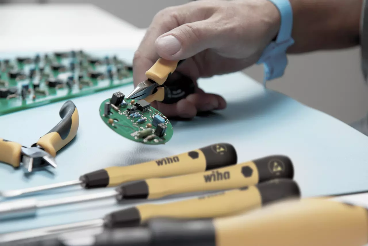 A person using pliers to work on a green circuit board with tools nearby.