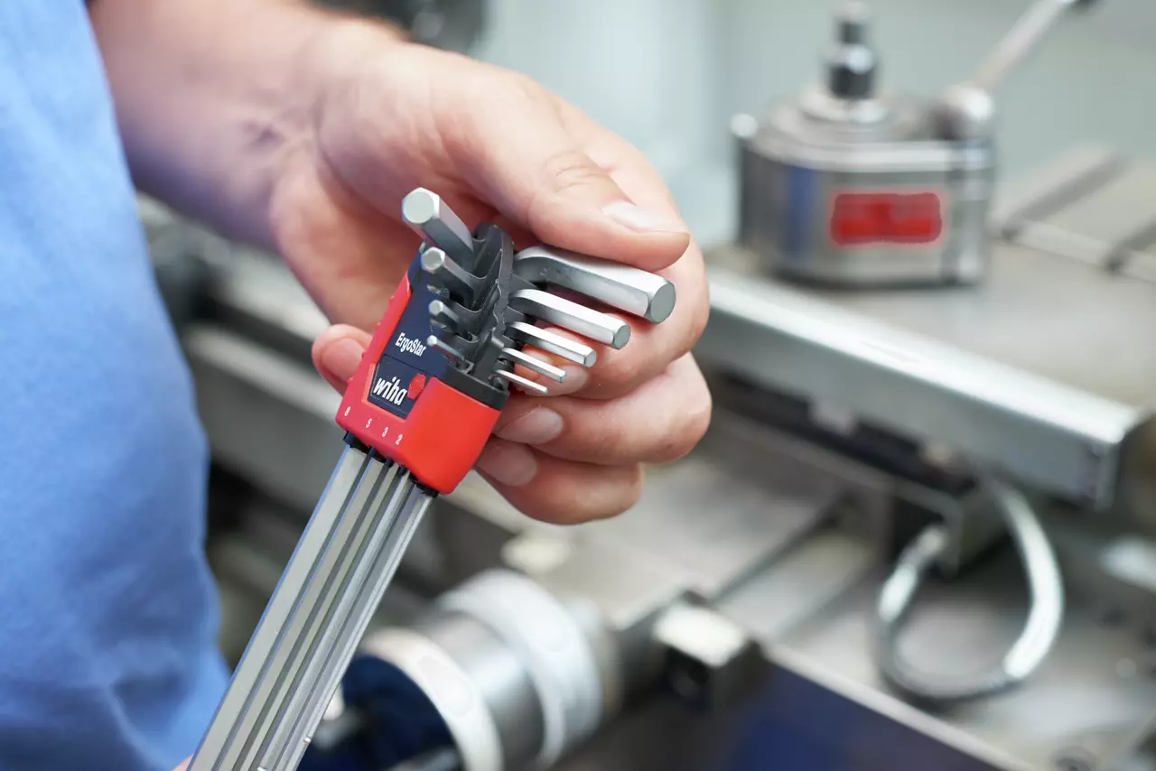 A person holds a set of hex keys in a red holder, with machinery in the background.