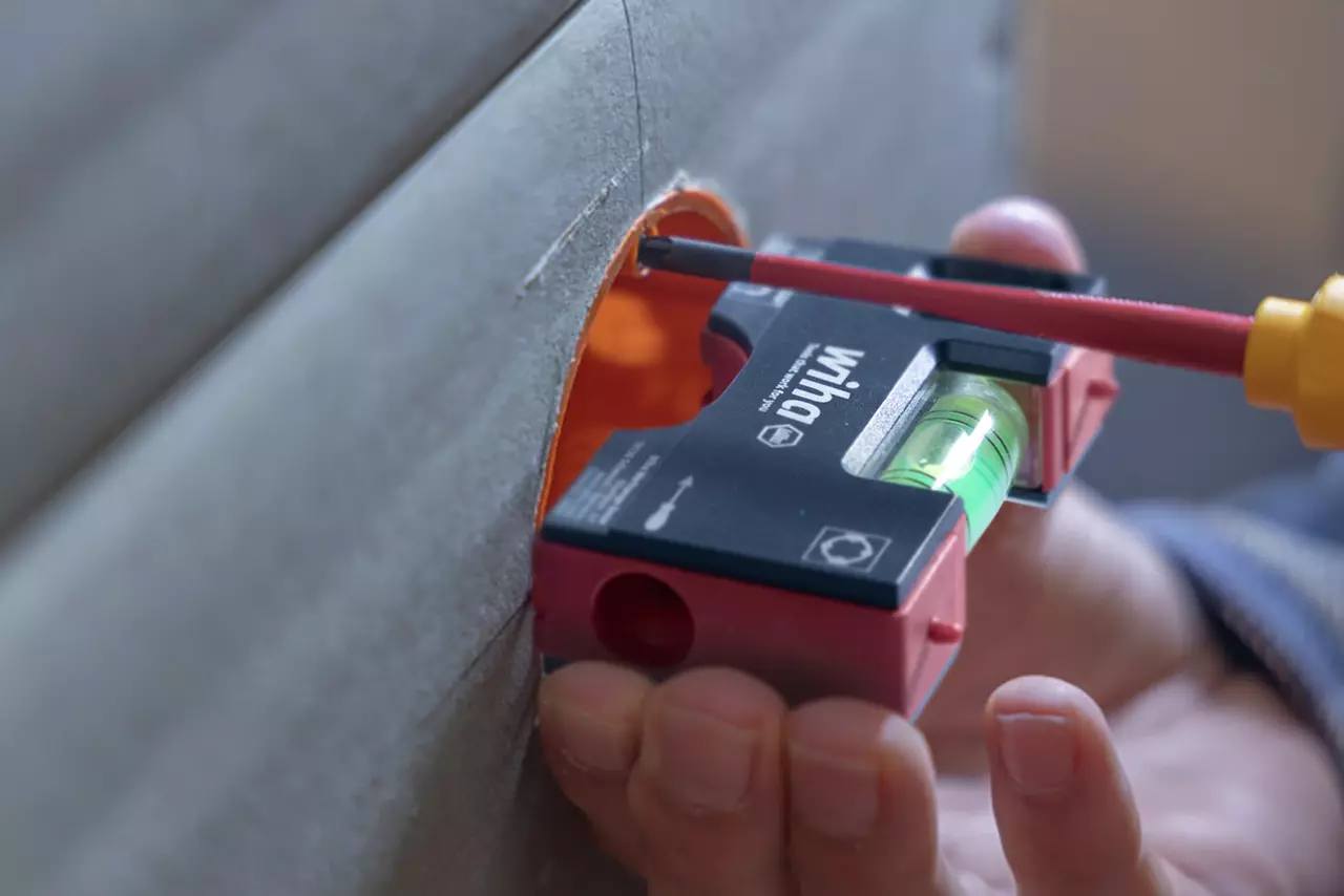 Person using a leveling tool and screwdriver on a wall socket