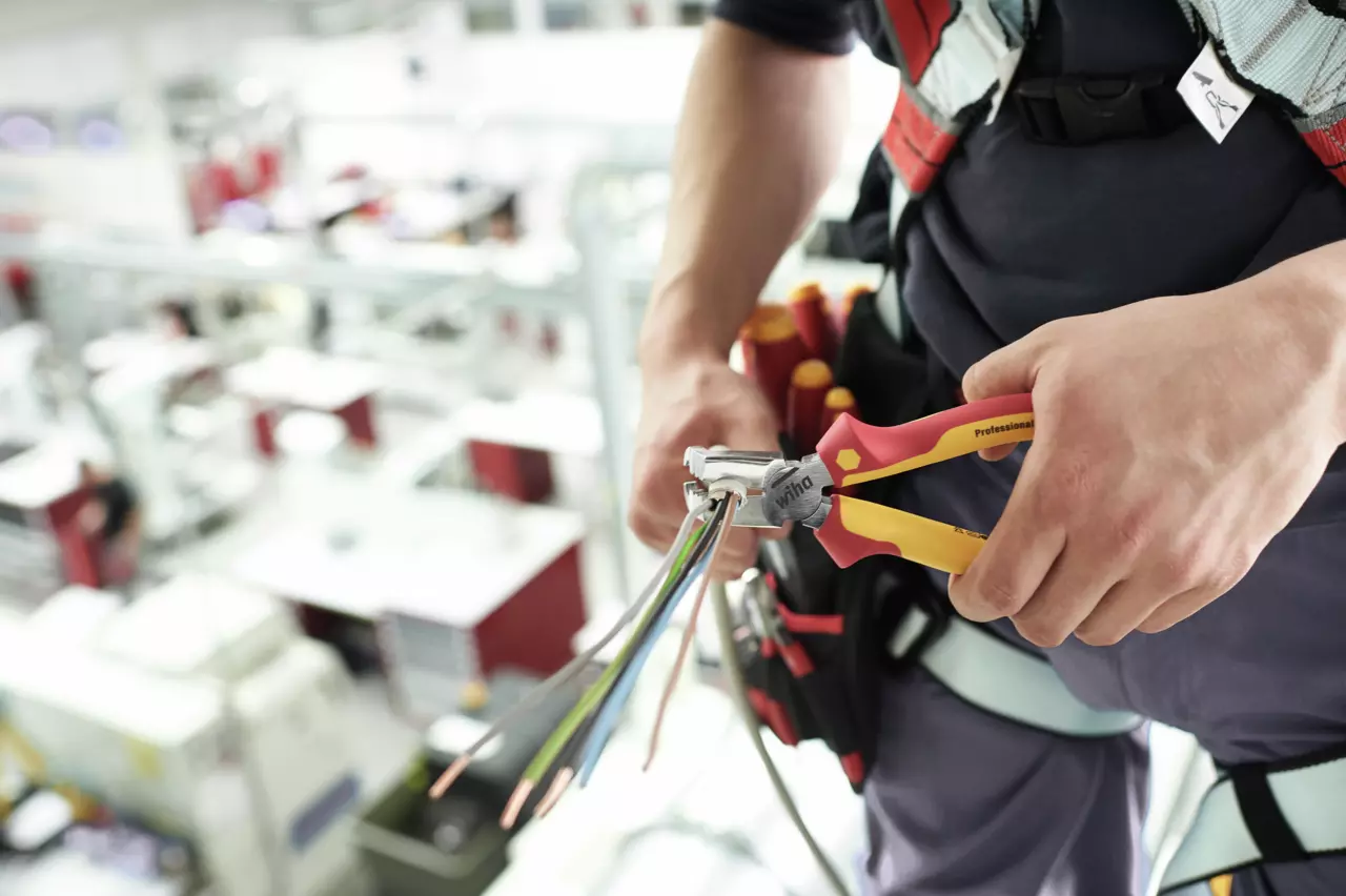 Person using pliers to cut electrical wires in a workshop setting.