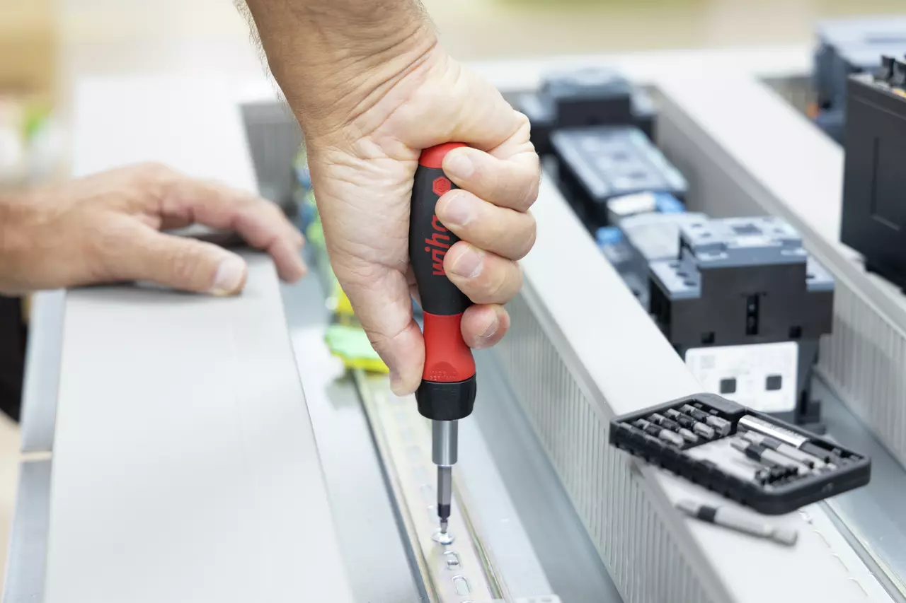 A person uses a red and black ratchet screwdriver on metal equipment