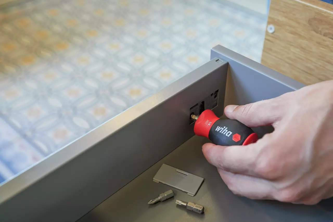 Hand using a stubby screwdriver to adjust a fitting in a drawer, with bits lying nearby.