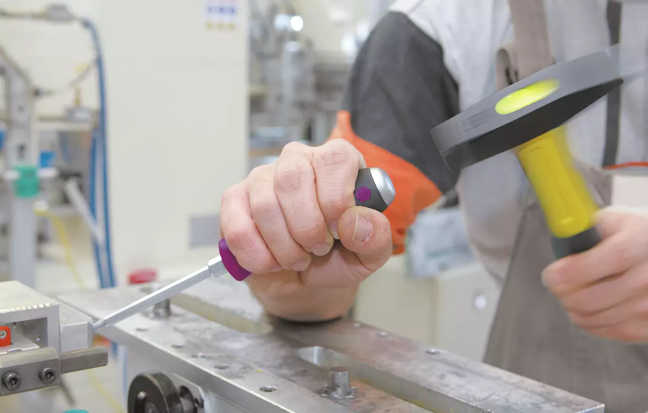 A person using a screwdriver and hammer on a metal surface in a workshop.