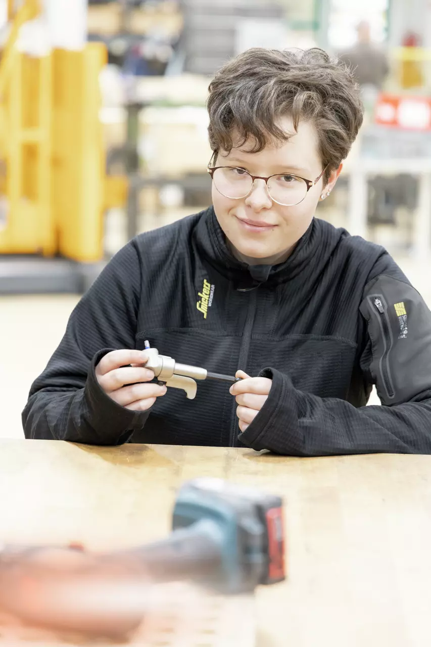 Person holding a small metal tool in hand at a table