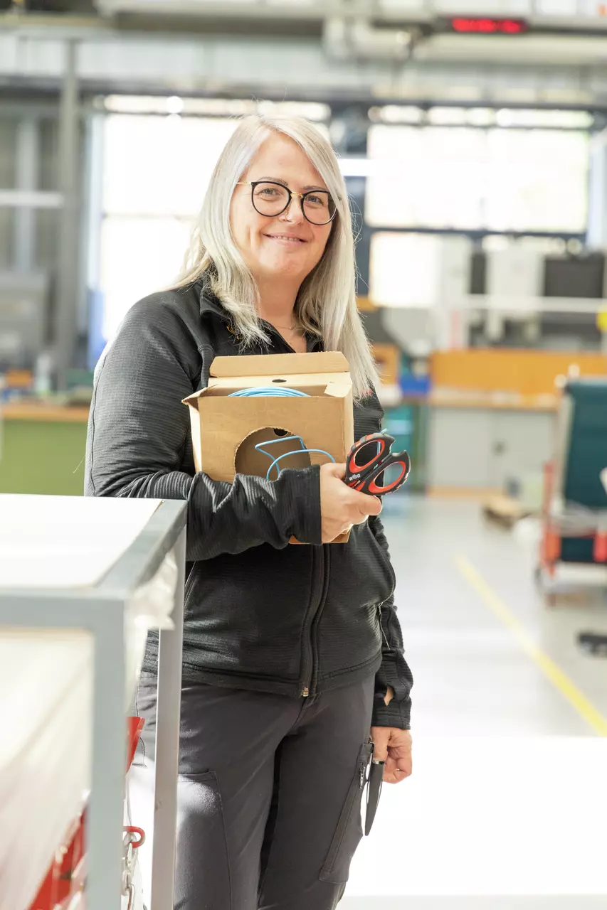 A person holding a cardboard box and a pair of scissors in a workspace.
