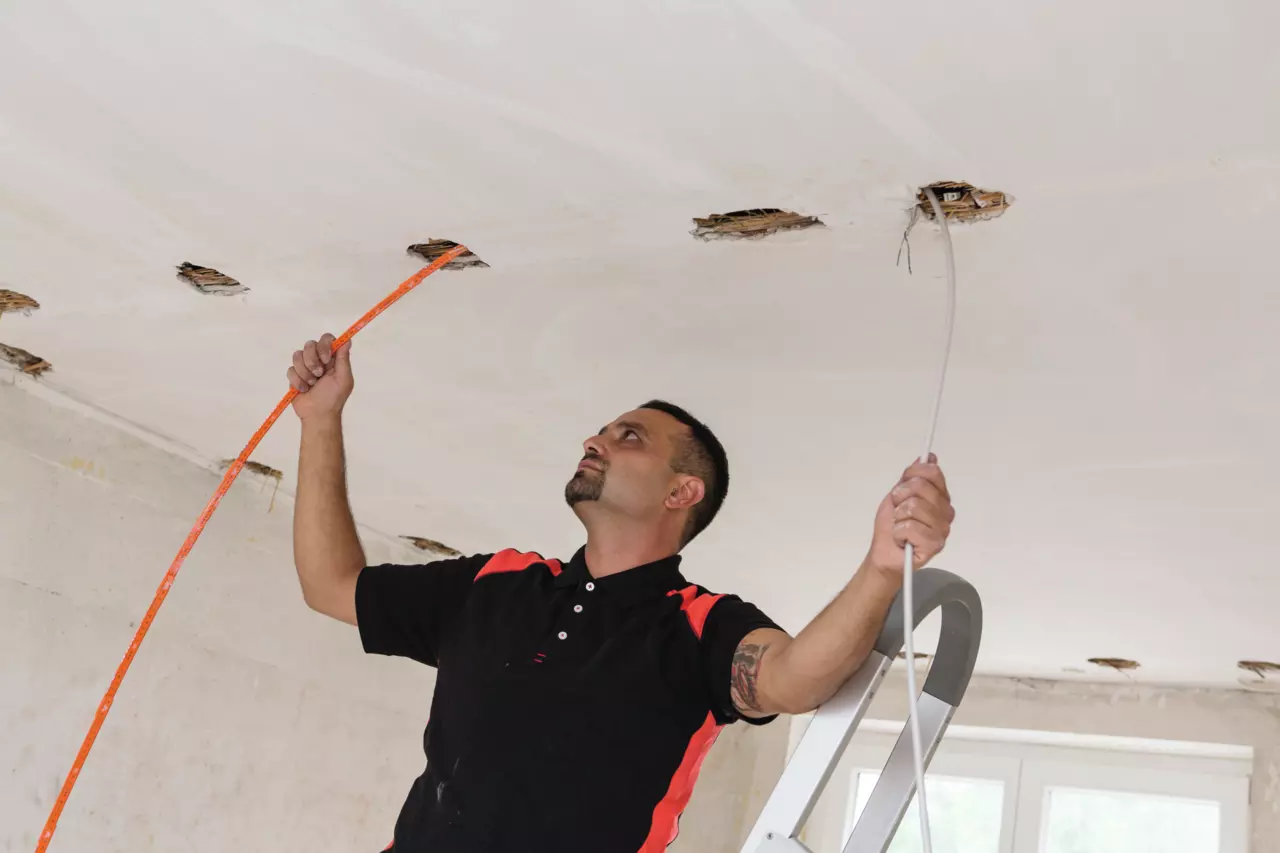 A man working on the ceiling with a folding ruler and cable