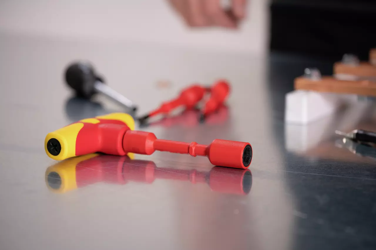 Red and yellow electric screwdriver on a metal surface with blurred tools in the background.