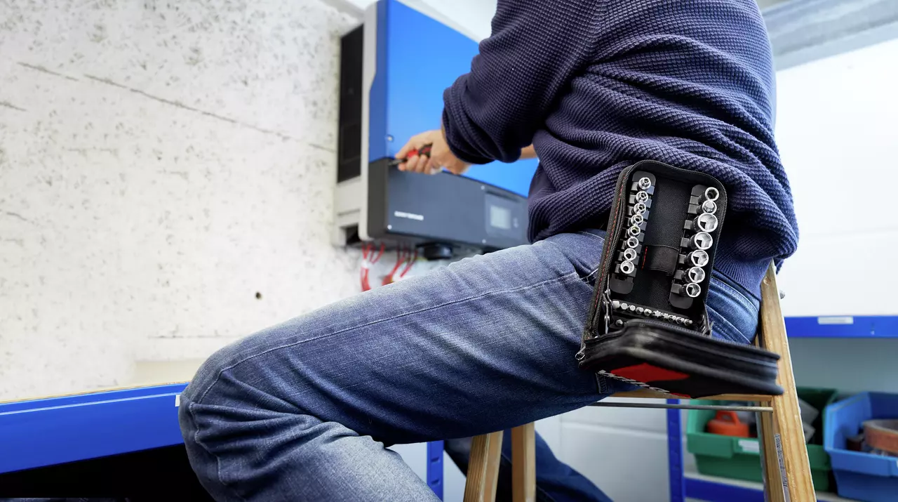 A person is working on a wall-mounted device with a socket set on their lap.