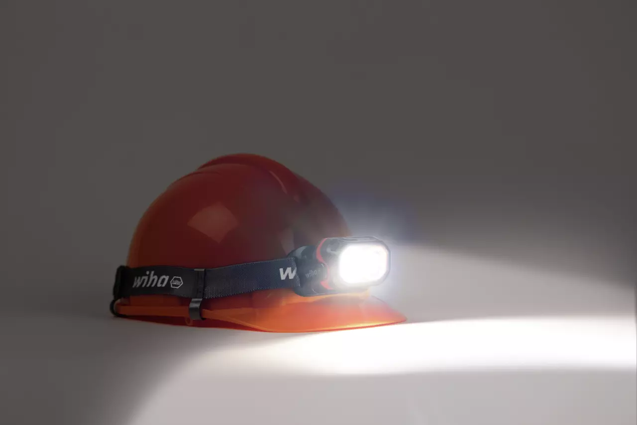 A red hard hat with an illuminated headlamp attached in a dark setting.
