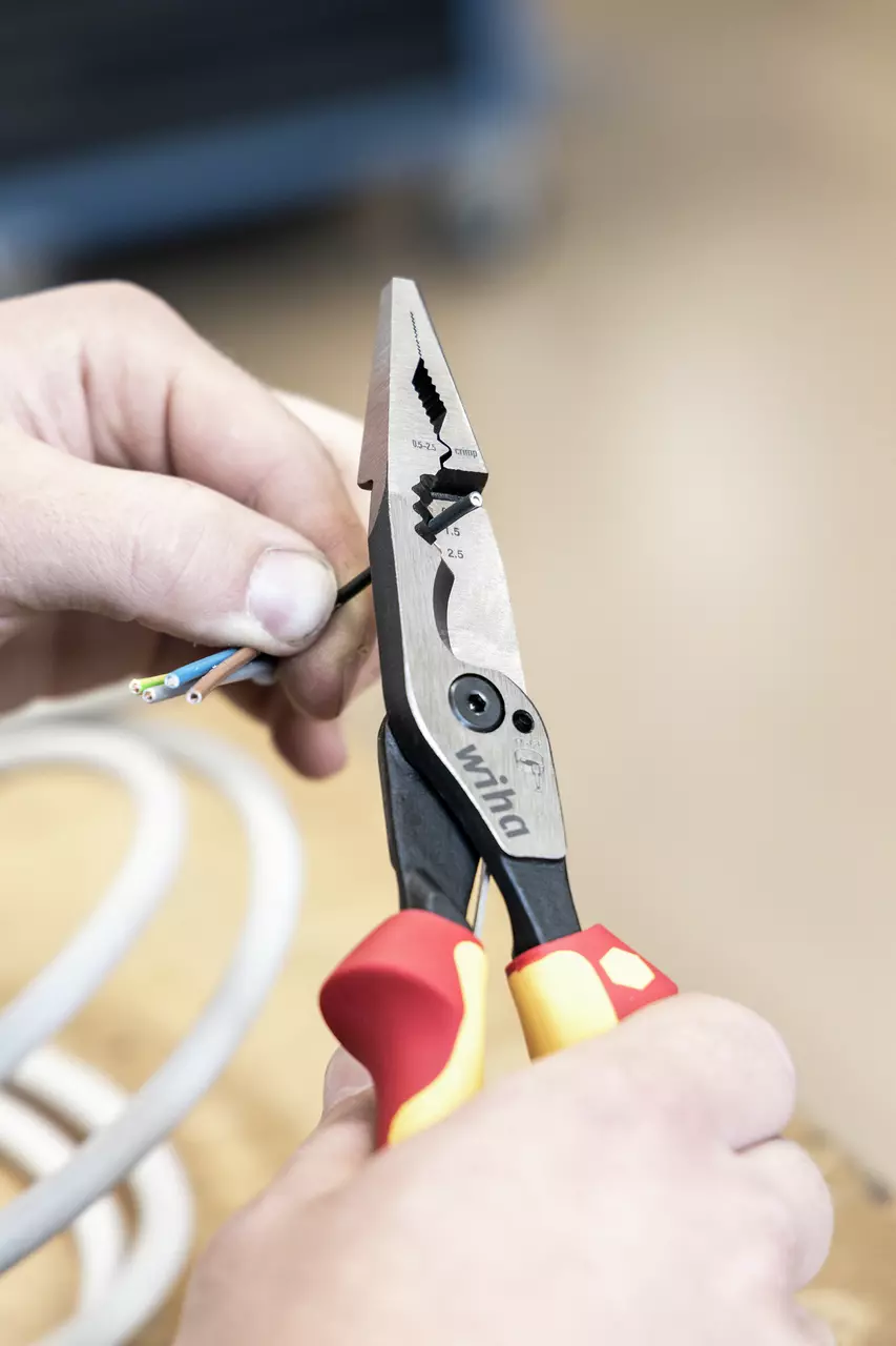 Person using pliers with red and yellow handles to strip insulation from electrical wires.