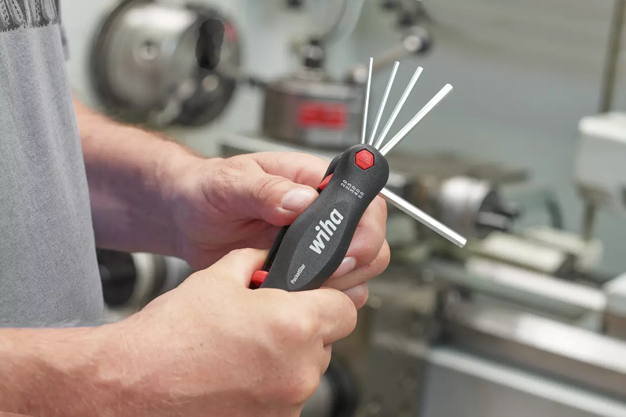 Person holding a foldable hex key set with multiple keys extended, standing in a workshop.