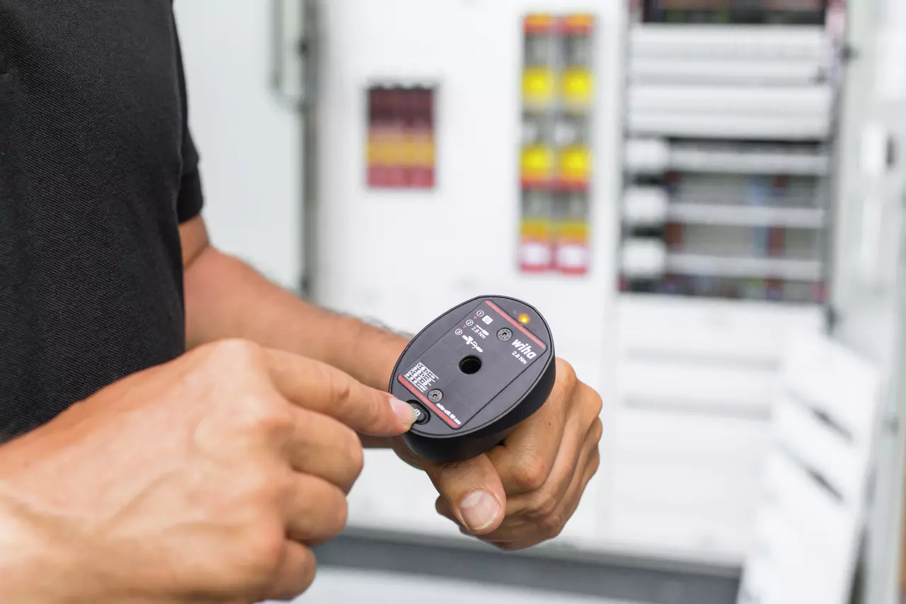 Person holding a torque measurement device in front of electrical panel