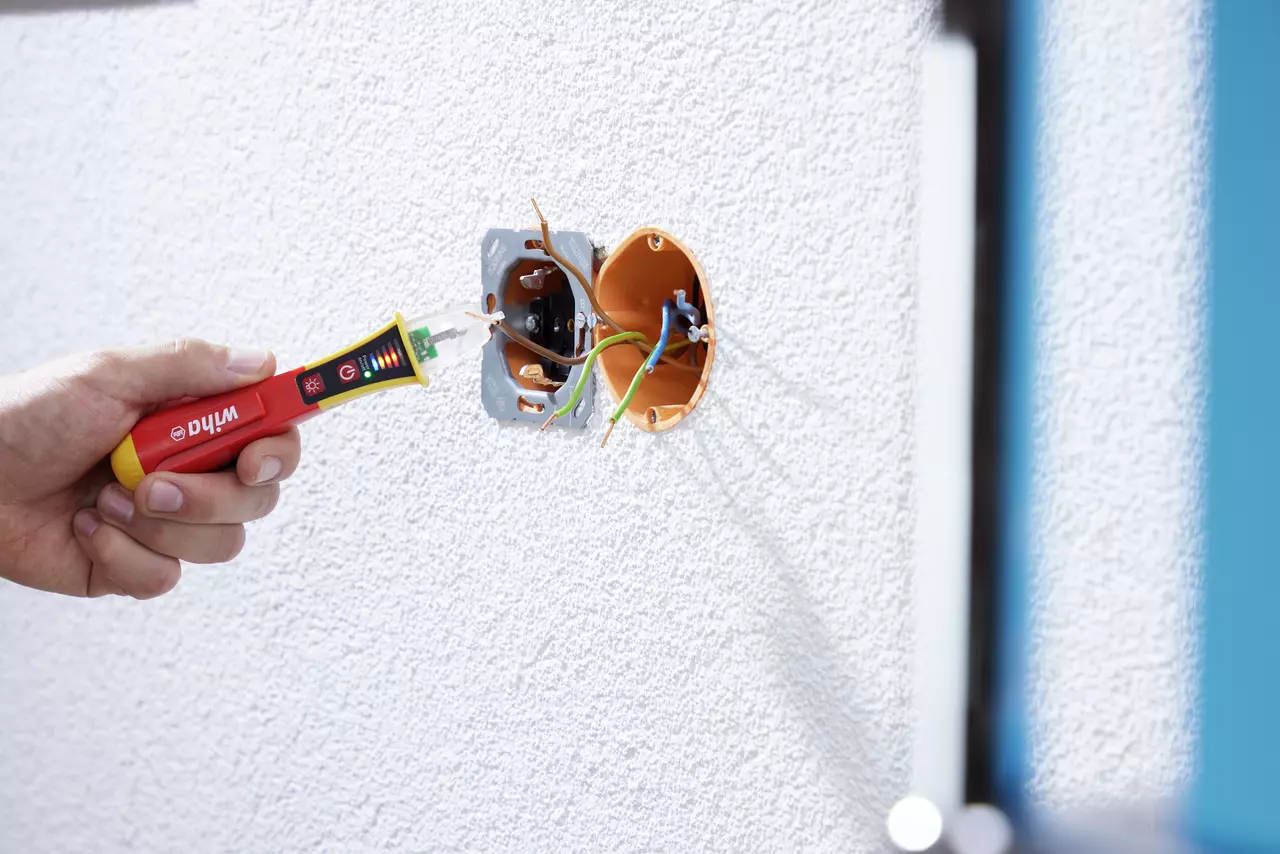 Hand using a non-contact voltage detector near exposed wires in a wall socket