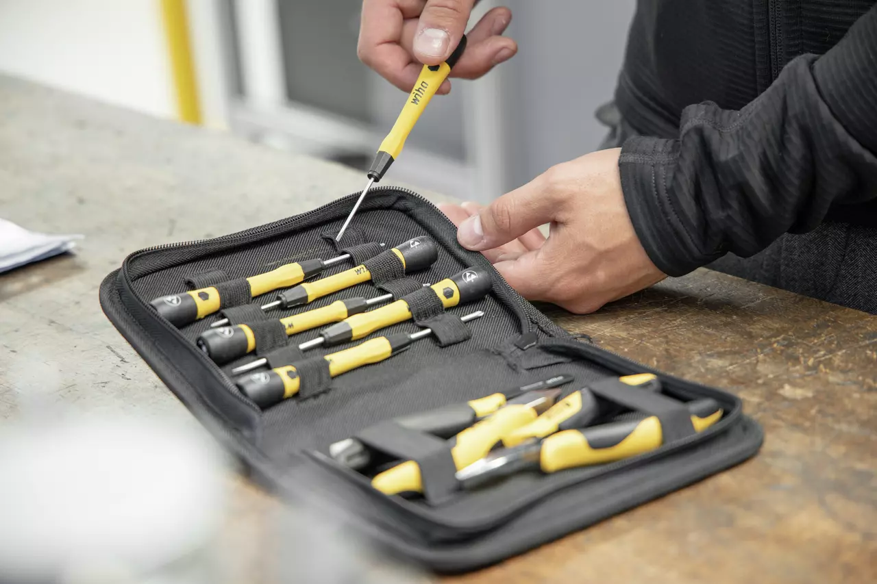 Person handling a yellow and black screwdriver from a tool set in a black case on a workbench.
