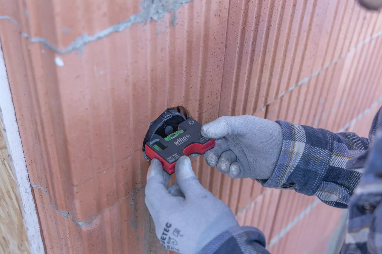Person using a small red level tool to align a cavity in a brick wall.