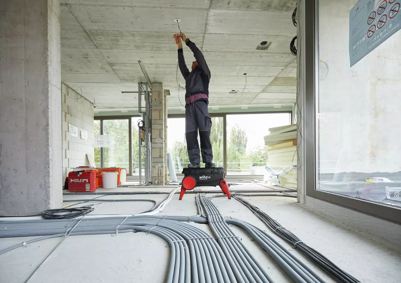 A person stands on a toolbox, working on a ceiling in a construction site.