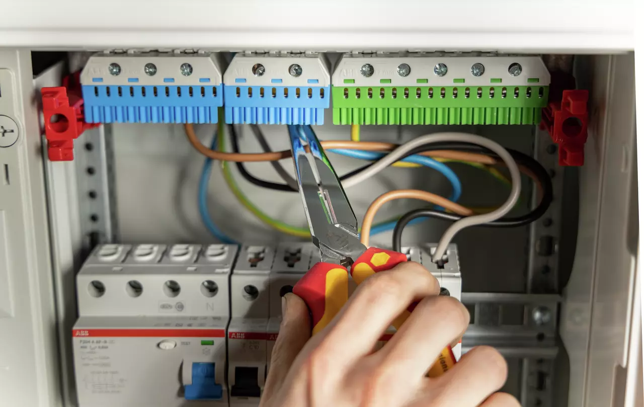 A person using needle-nose pliers to adjust wires in an electrical panel.
