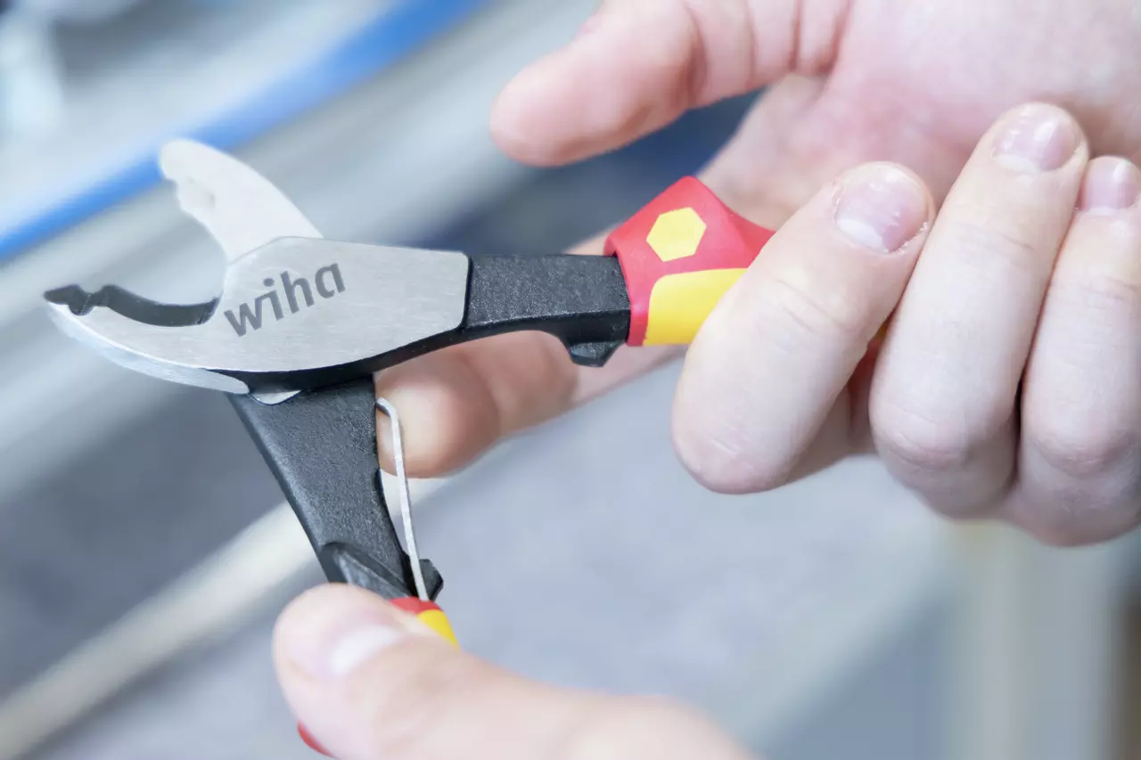 Person holding an industrial electric cable cutter with red and yellow handles