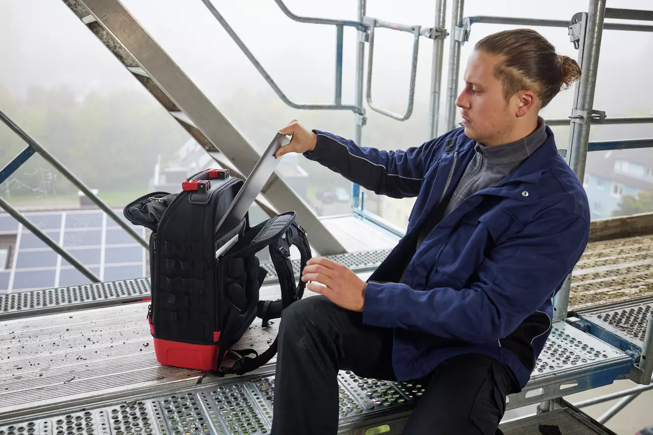 Person on scaffolding placing a laptop into a black backpack.