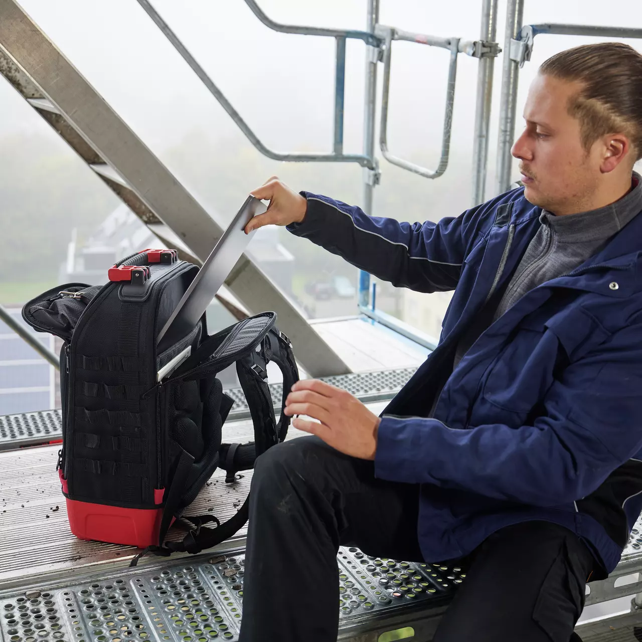 Person on scaffolding placing a laptop into a black backpack.