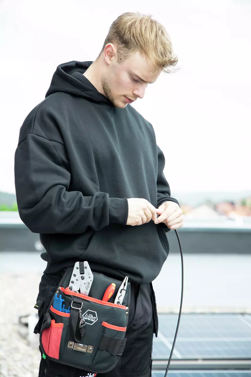 En person arbejder med en kabel på et tag og bærer et værktøjsbælte med forskellige værktøjer.