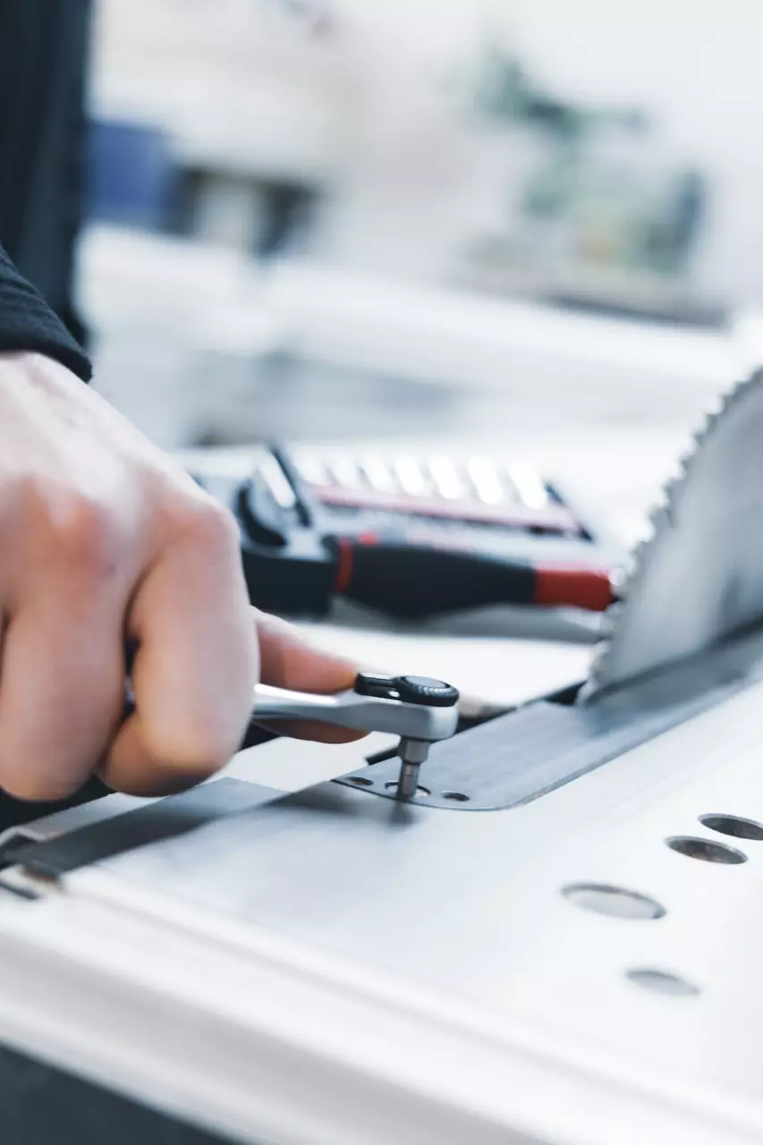 Person using a ratchet wrench to tighten a bolt on a metal surface near a circular saw blade.
