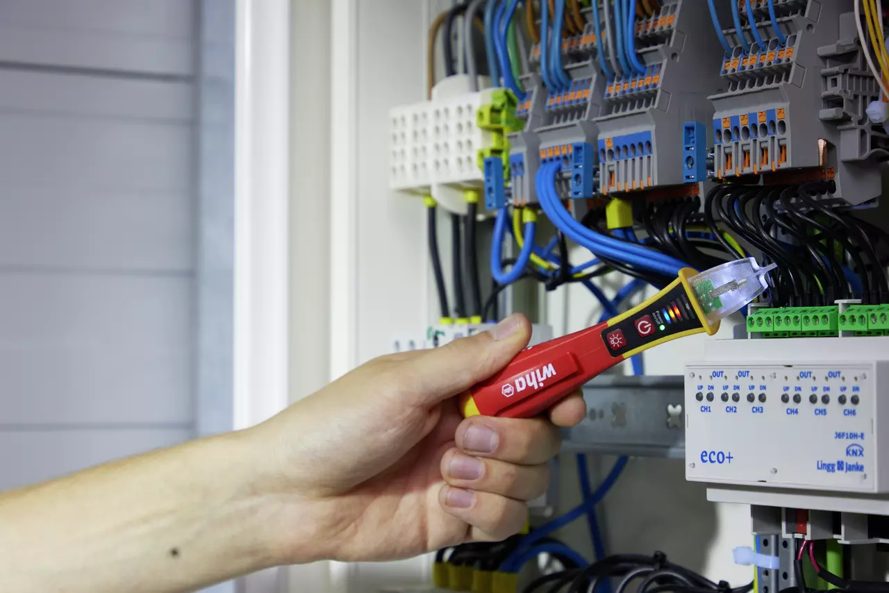 Hand holding a red non-contact voltage detector near wires in an electrical cabinet.