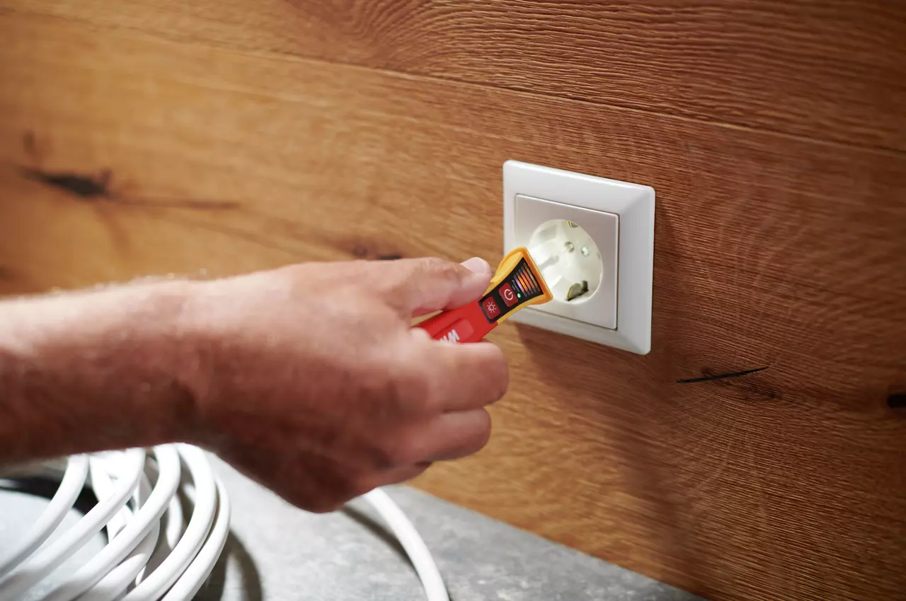 A person using a non-contact voltage detector on an electrical outlet.