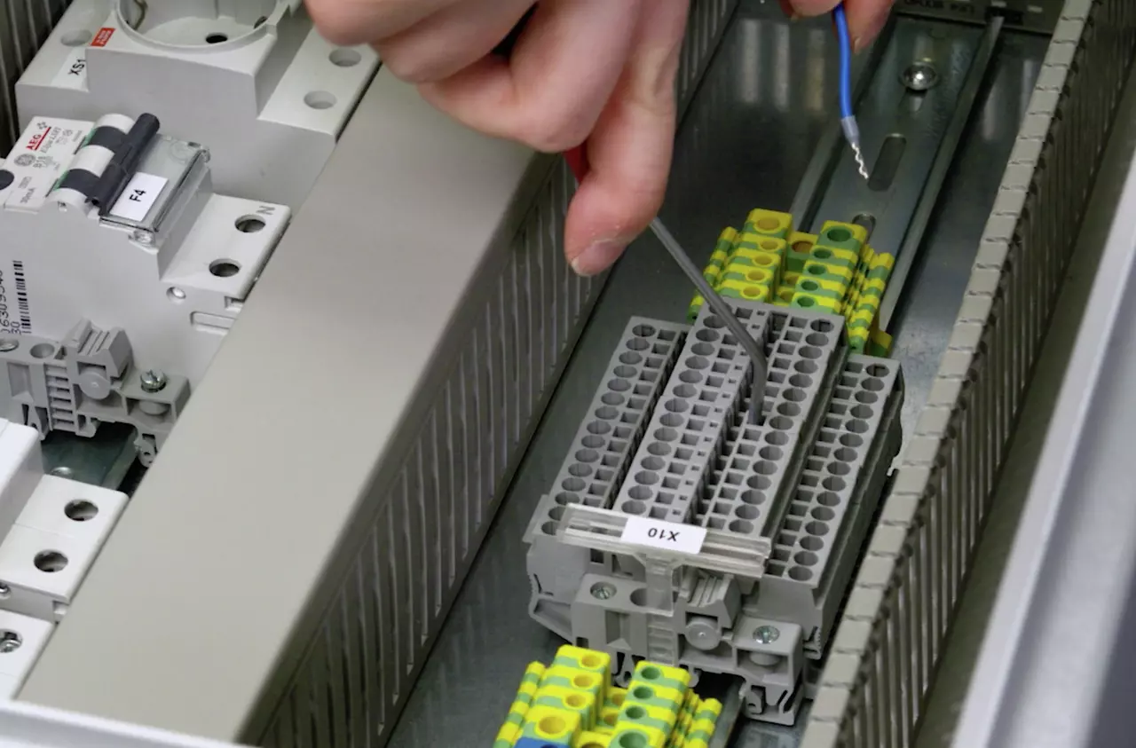A person uses a terminal actuation tool on a grey terminal block in an electrical panel.