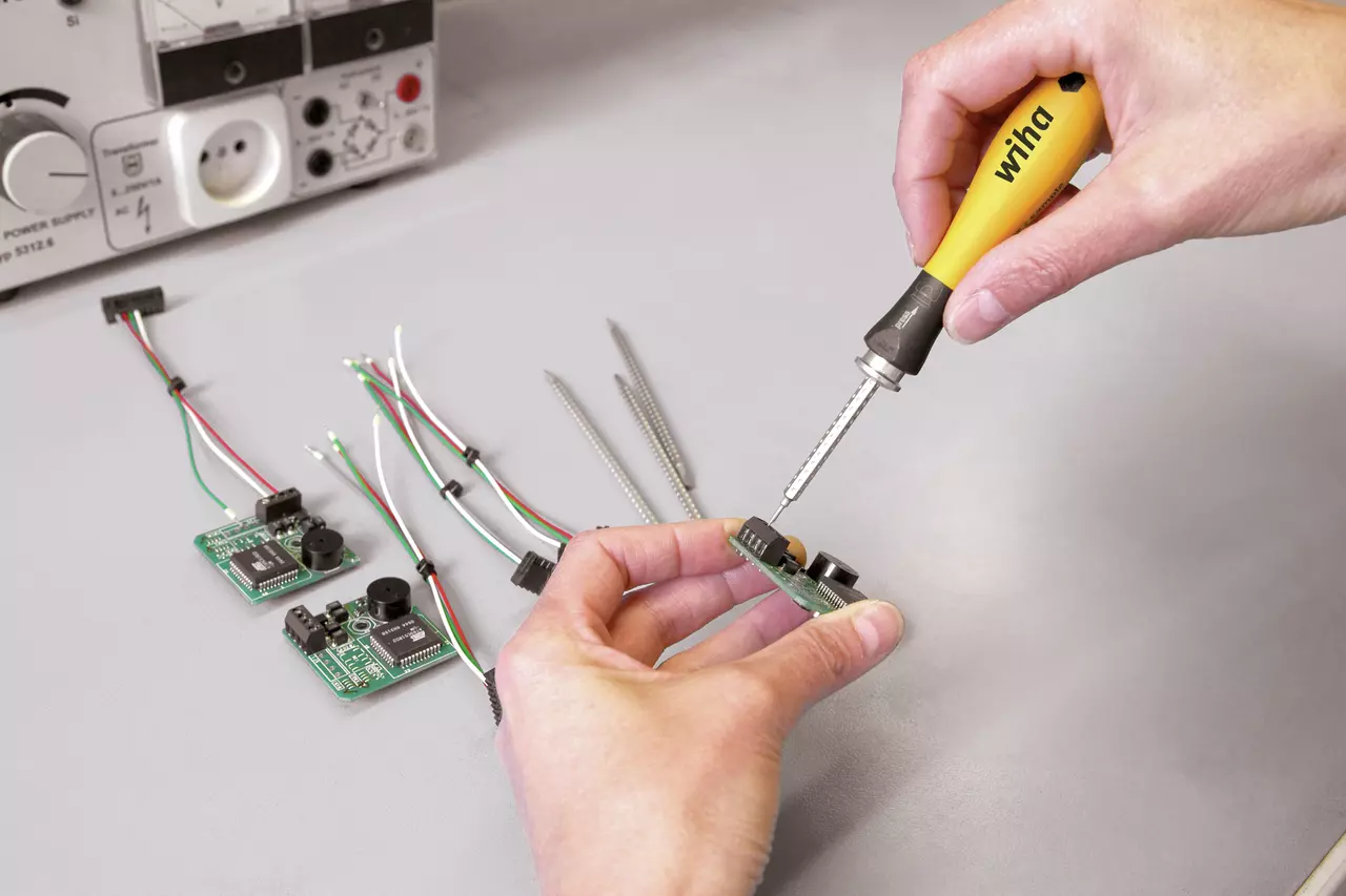 Person using a soldering iron on a circuit board with wires on a table.