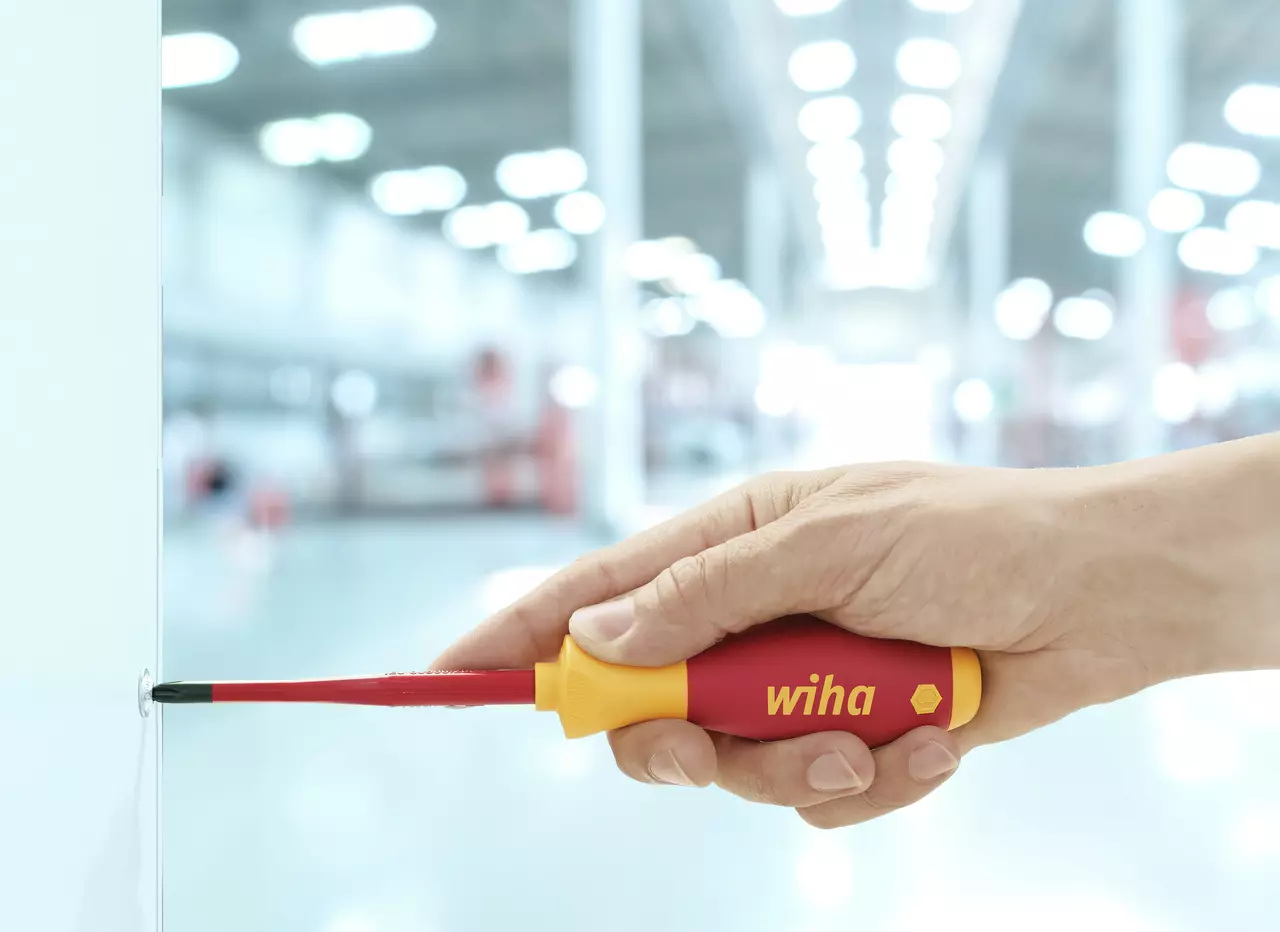 Hand using red and yellow screwdriver on a screw