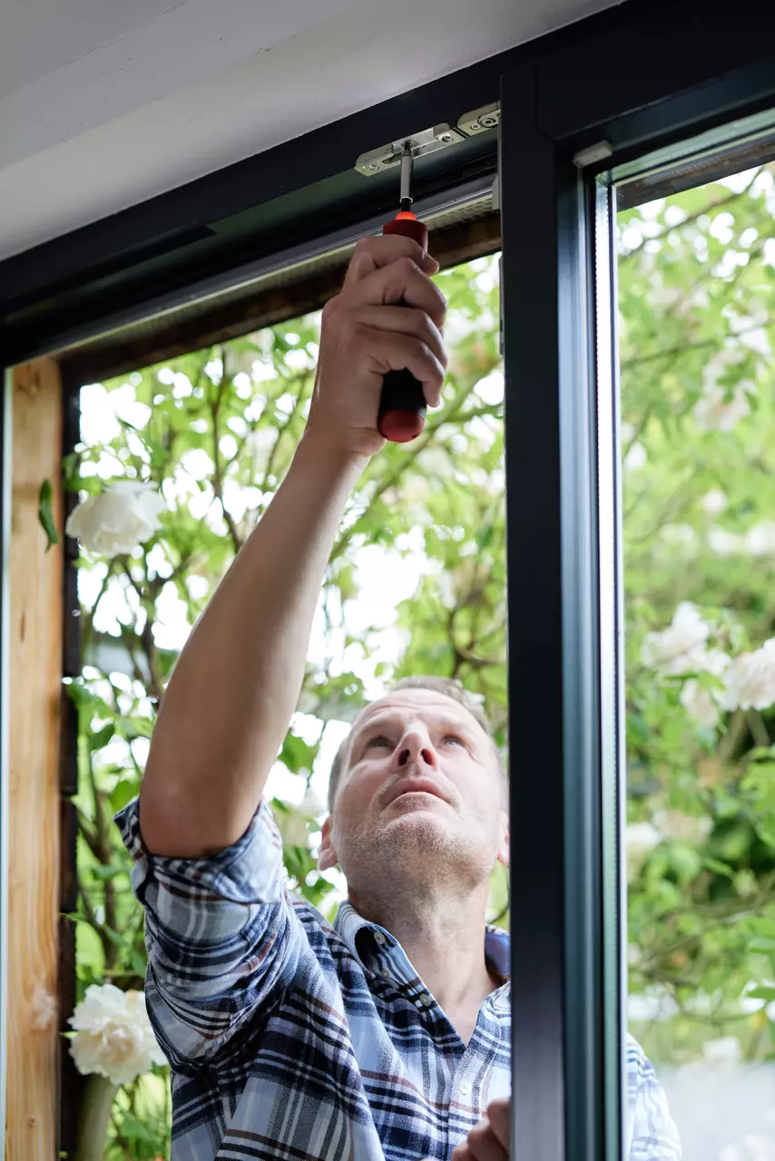 A person adjusts a window with a screwdriver.