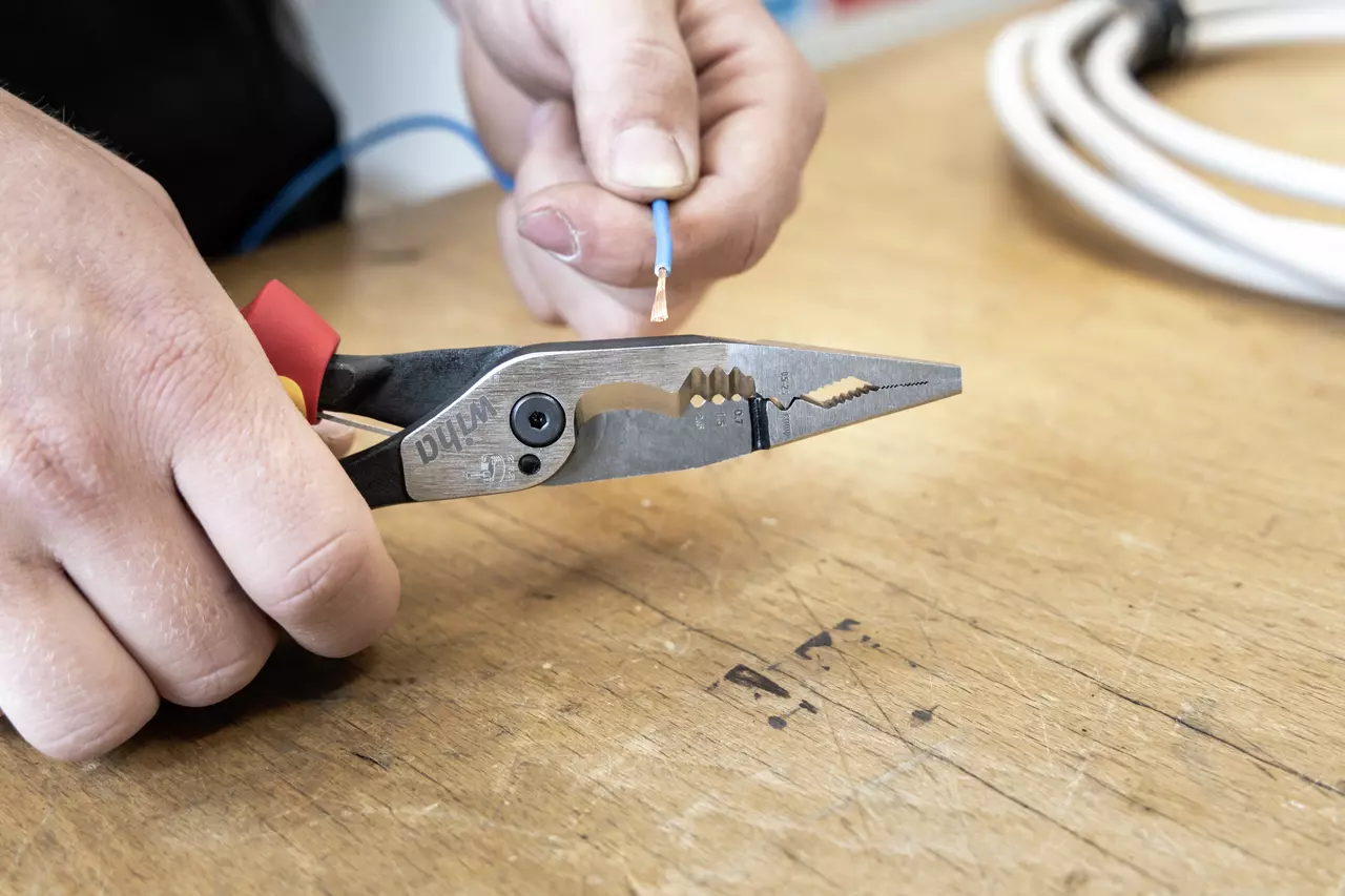 Persoon houdt een striptang en een kabel op een houten oppervlak