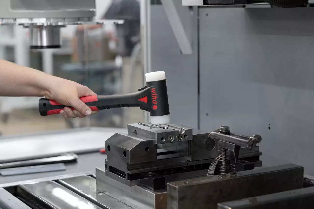 Eine Person nutzt einen Schonhammer auf einem Metallwerkstück in einer Werkstatt.