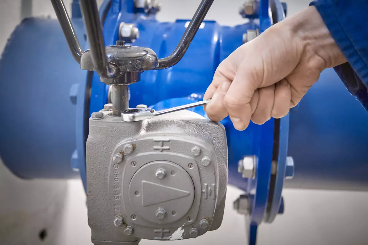 A person uses a ratchet wrench on a metallic valve connected to a large blue pipe.