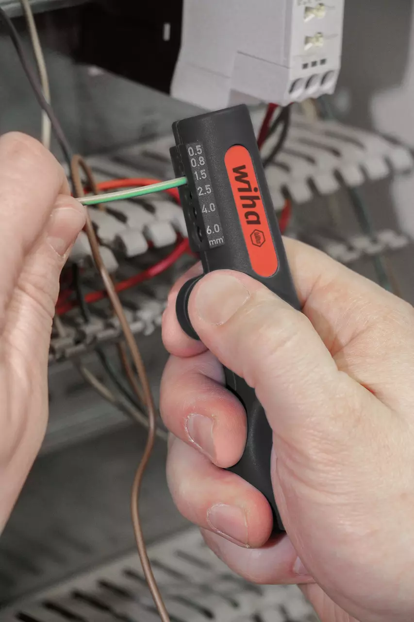 A person using a black and red wire stripping tool on a green wire in an electrical setup.