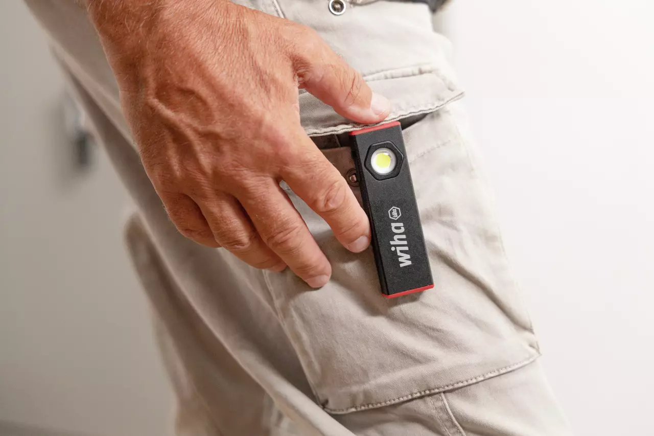 A person clips a small black and red flashlight to their beige pants pocket.