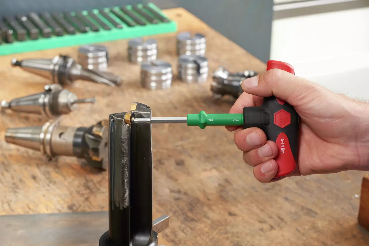 Person using a torque screwdriver on a tool piece, with various metal parts in the background.