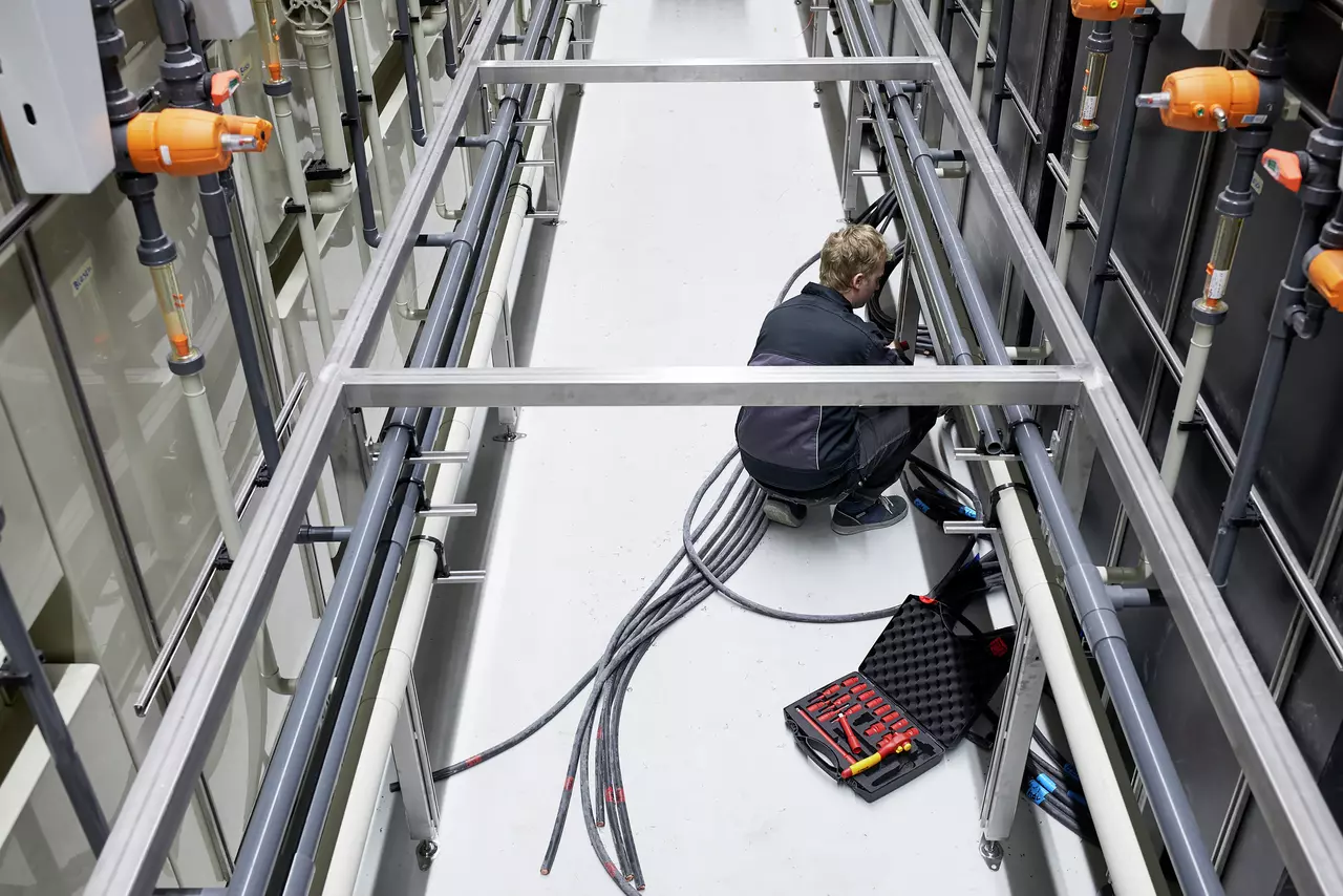 A person working with cables and tools in an industrial setting. Tool case open nearby.
