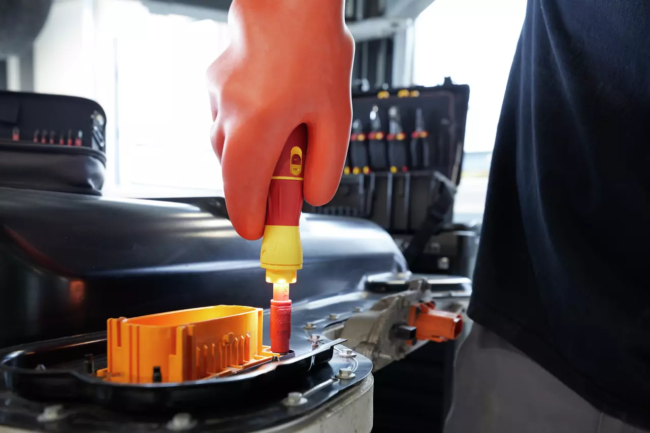 Person using an electric screwdriver on a car battery with orange gloves