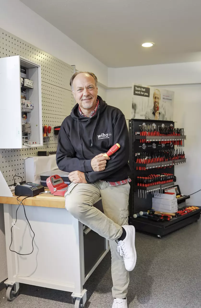 Een persoon in een zwarte hoodie houdt een schroevendraaier vast in een werkplaats