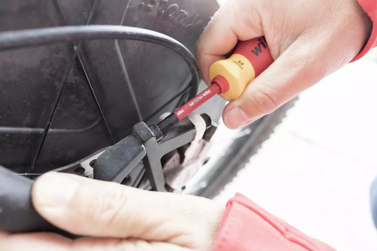Person using an electric screwdriver to adjust a bicycle brake cable.